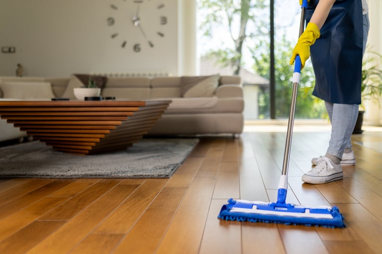 A person wearing yellow gloves uses a mop to wipe hardwood floors in a stylish living room